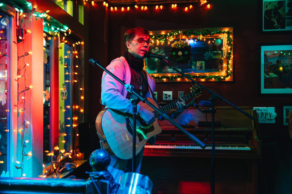 AVS student performing at the Bebop open mic with guitar in hand and standing at mic.